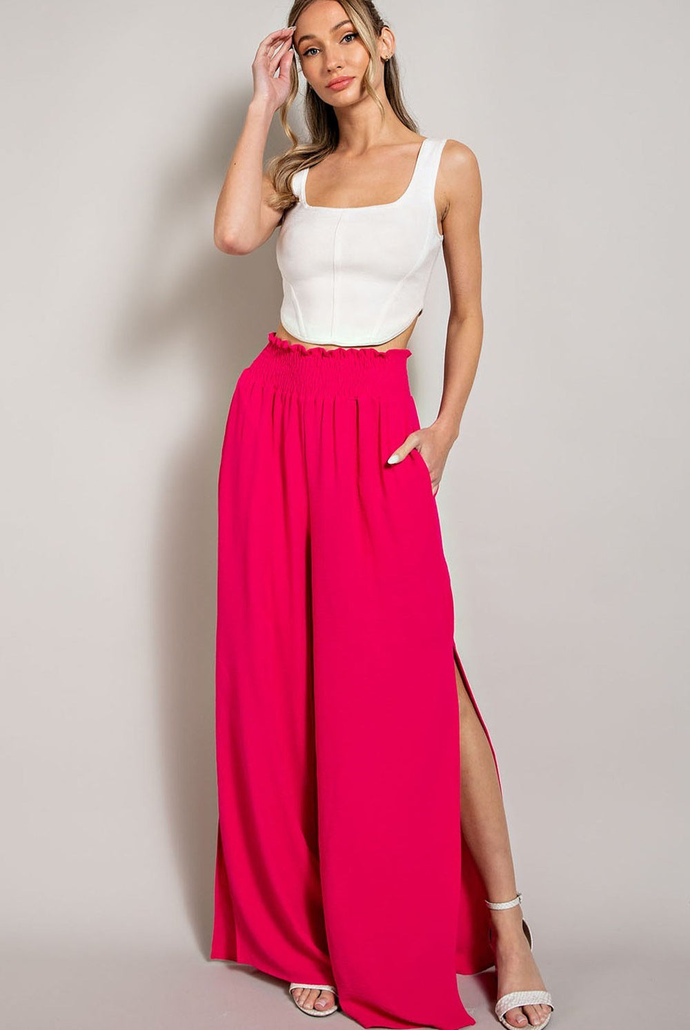 Woman wearing a white top and bright pink wide-leg pants on a plain background