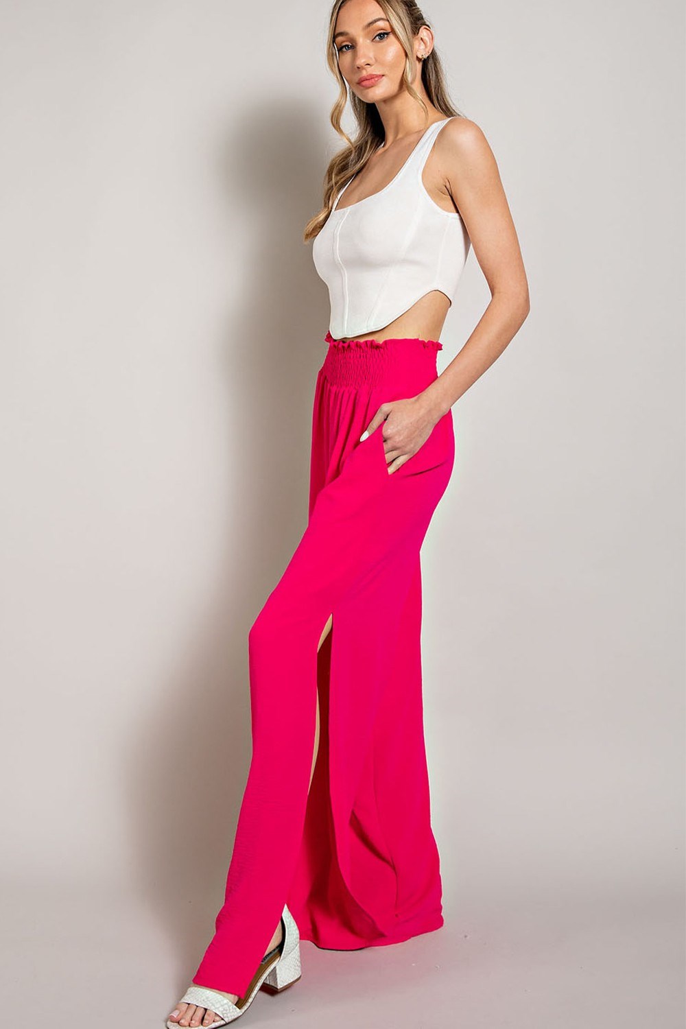 Woman wearing a white top and bright pink pants against a plain background