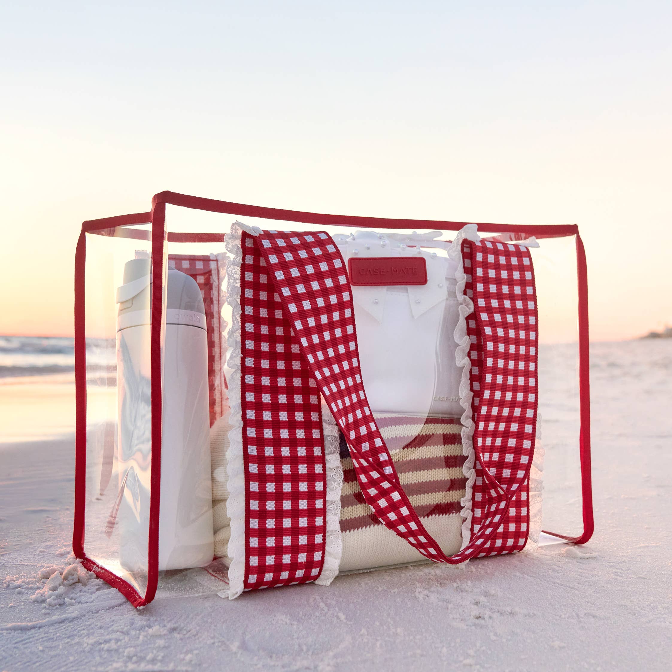 Clear beach bag with red checkered strap on a sandy beach