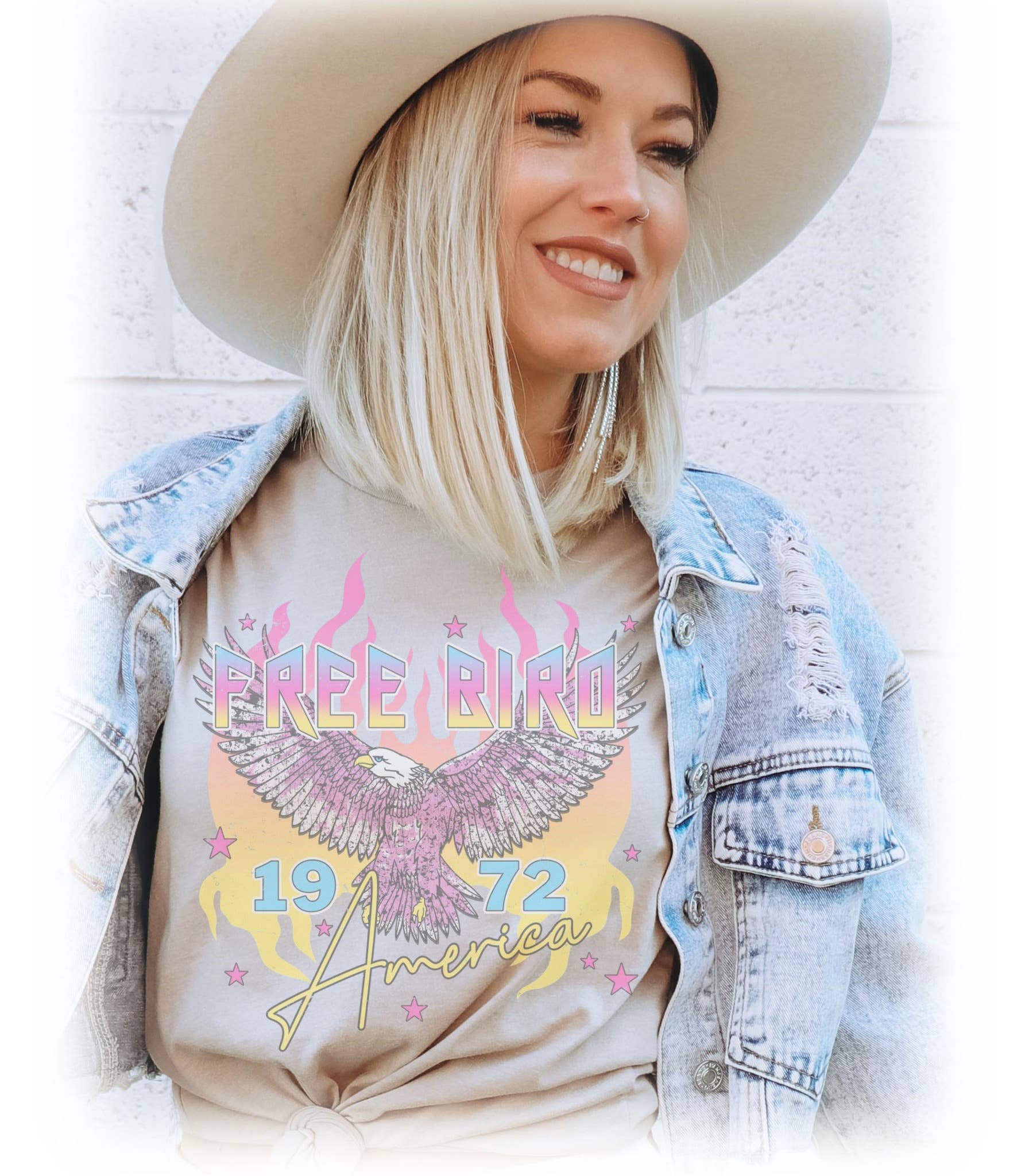 Woman wearing a t-shirt with 'Free Bird America 1972' design, denim jacket, and cowboy hat.