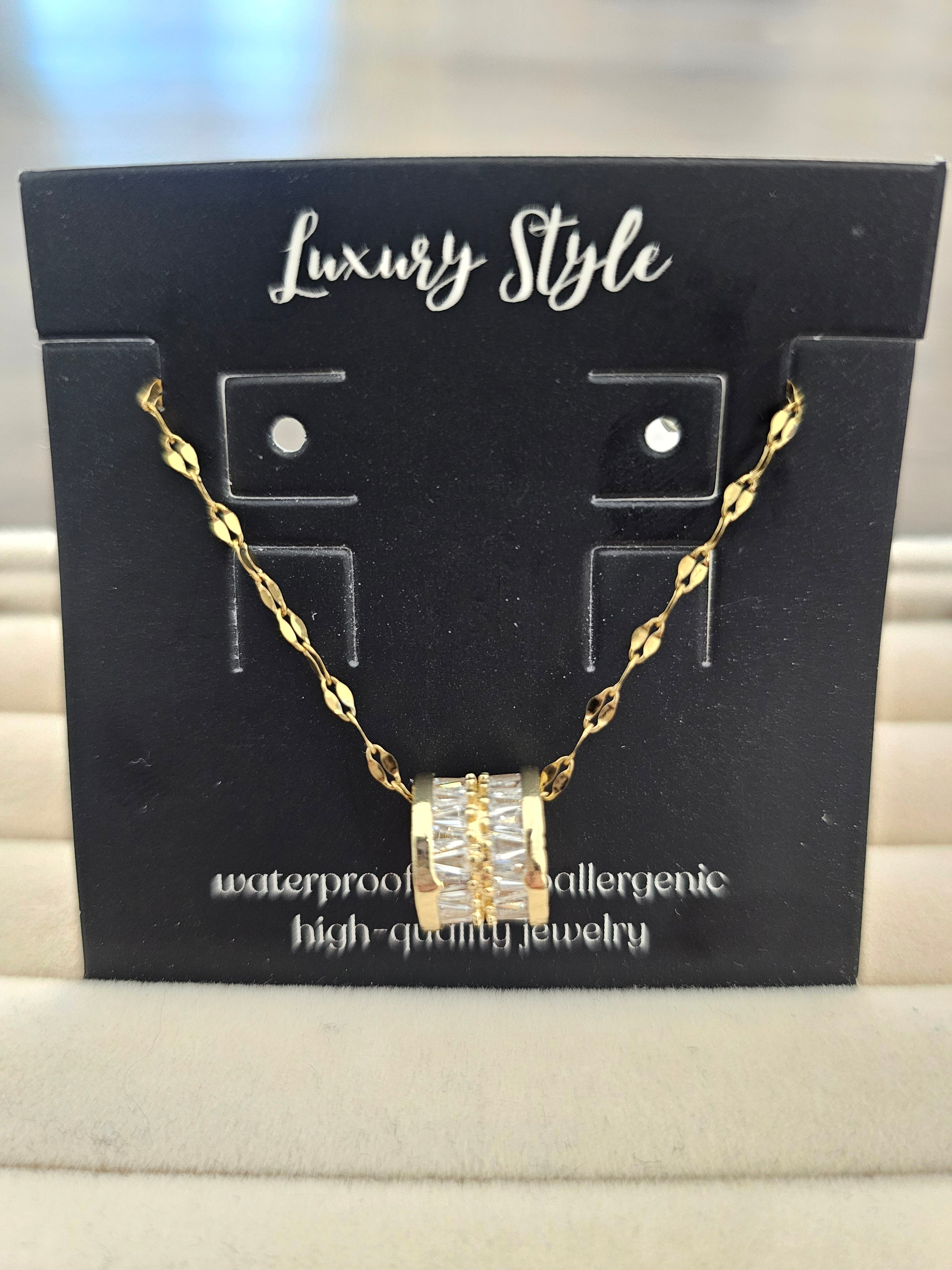 A gold chain necklace with a rectangular pavé-set stone pendant, displayed on a black card labeled 'Luxury Style'.