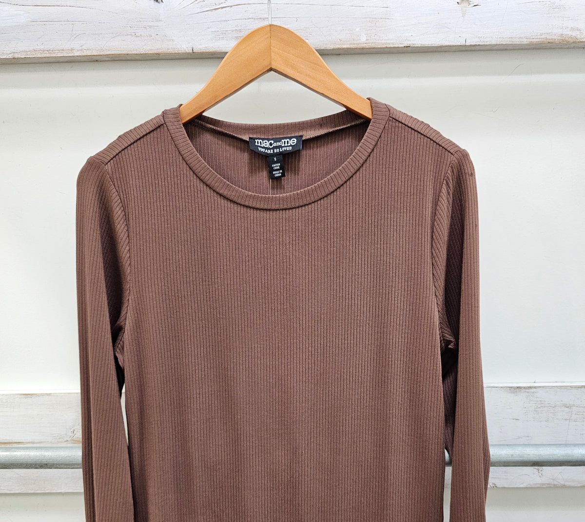 A brown ribbed long-sleeve top hanging on a wooden hanger against a white paneled wall.