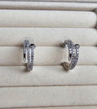 Pair of nail silver hoop earrings with clear stones on a beige jewelry display.