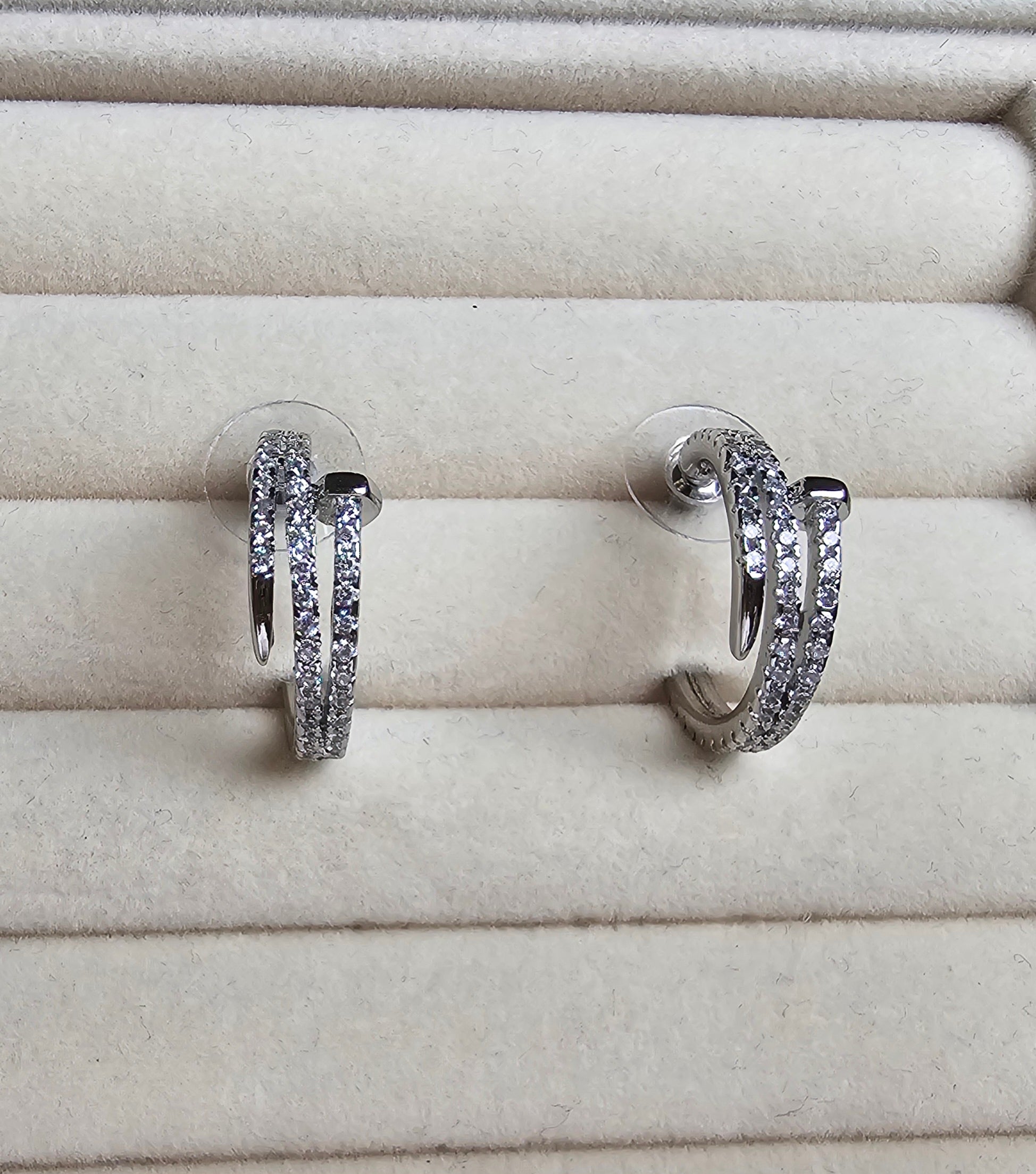 Pair of nail silver hoop earrings with clear stones on a beige jewelry display.
