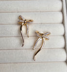 Gold bow-shaped earrings on a textured beige surface