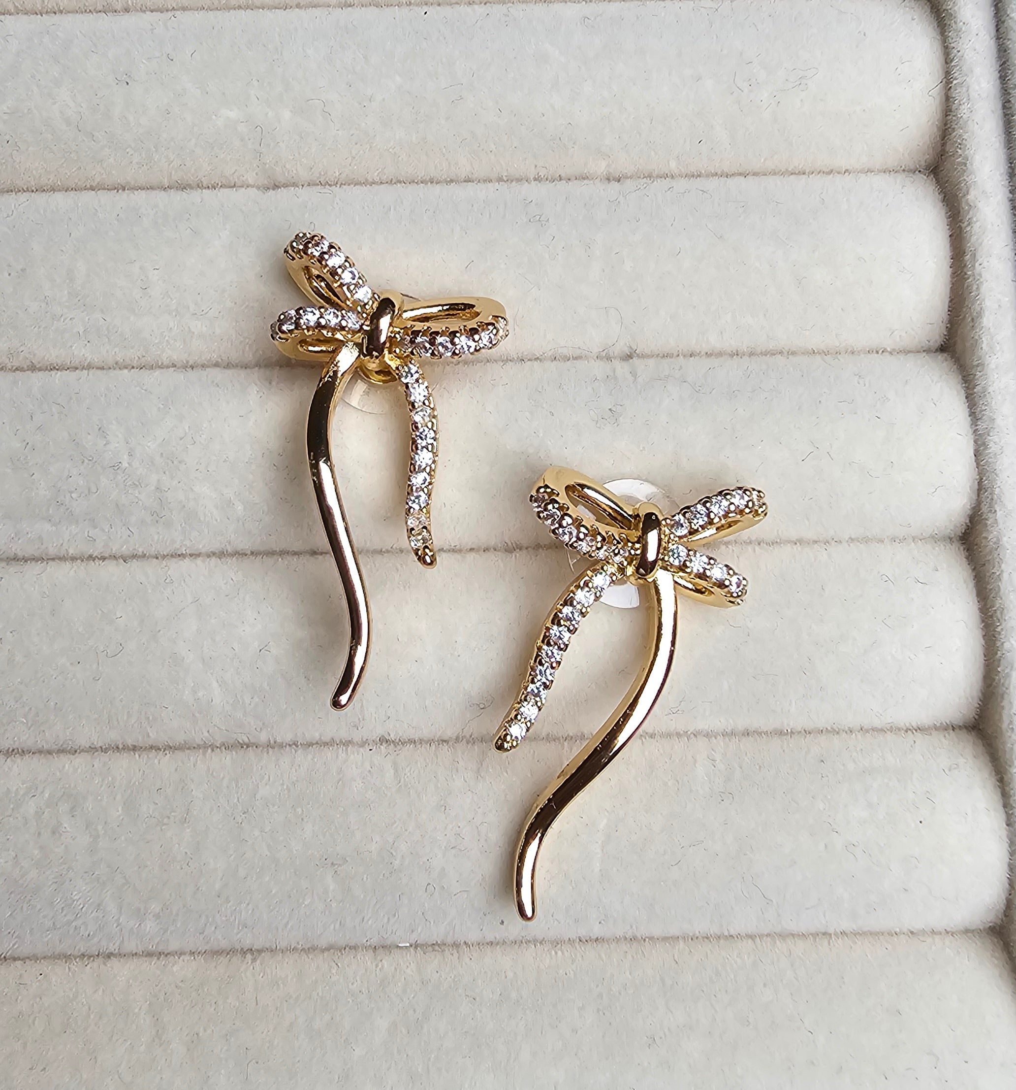 Gold bow-shaped earrings on a textured beige surface