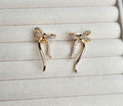 Gold bow-shaped earrings with rhinestones on a light gray surface