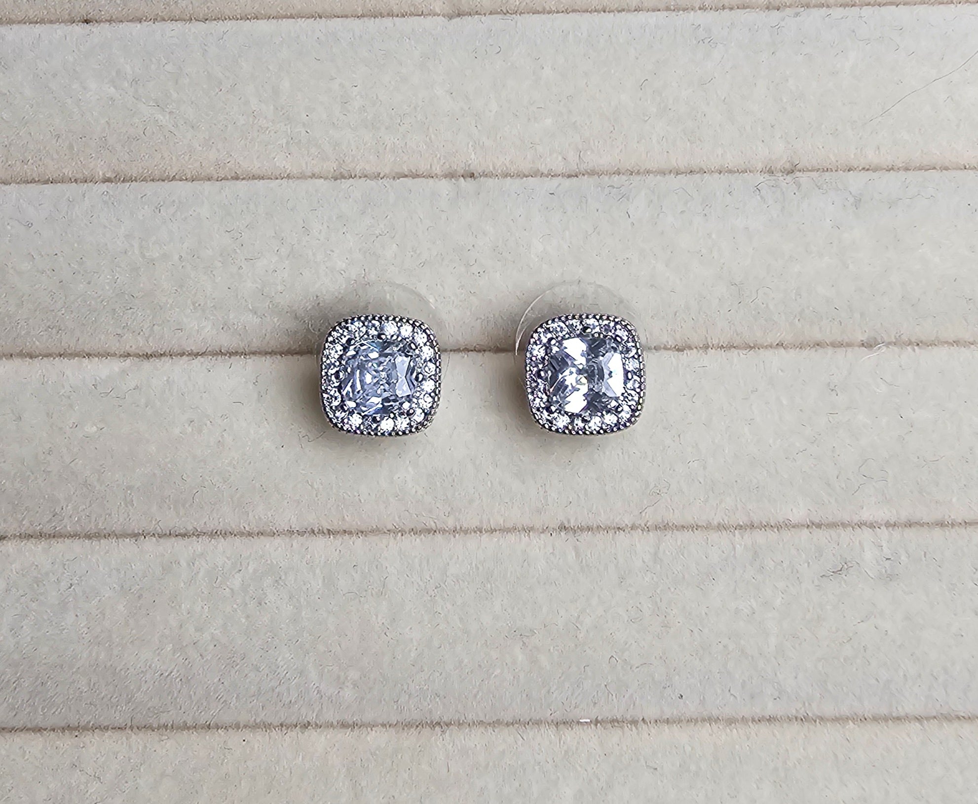 Pair of silver stud earrings with clear gemstones on a light gray surface