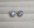 Silver square earrings with clear gemstones on a beige surface