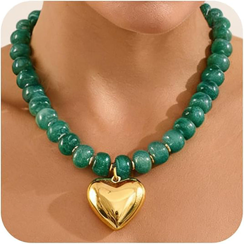 A green beaded necklace with a shiny gold heart-shaped pendant, shown on a model's neck.