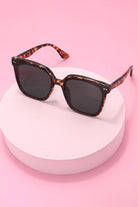 Sunglasses with tortoiseshell frame on a white stand against a pink background