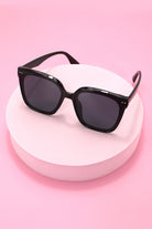 Black sunglasses on a white stand against a pink background