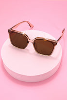 Sunglasses with brown lenses and gold frames on a pink background