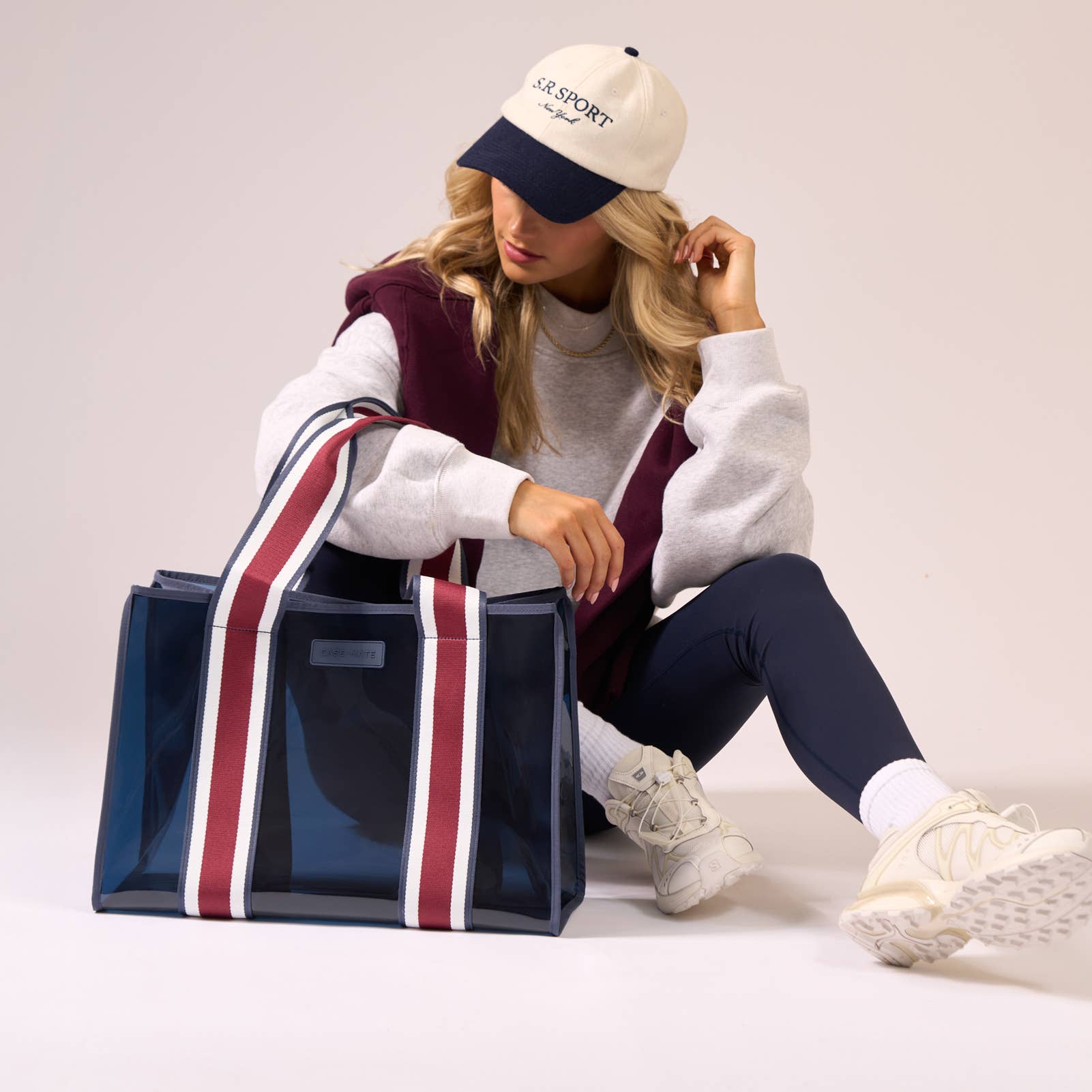 Woman sitting with a large blue tote bag, wearing a white cap and colorful outfit.