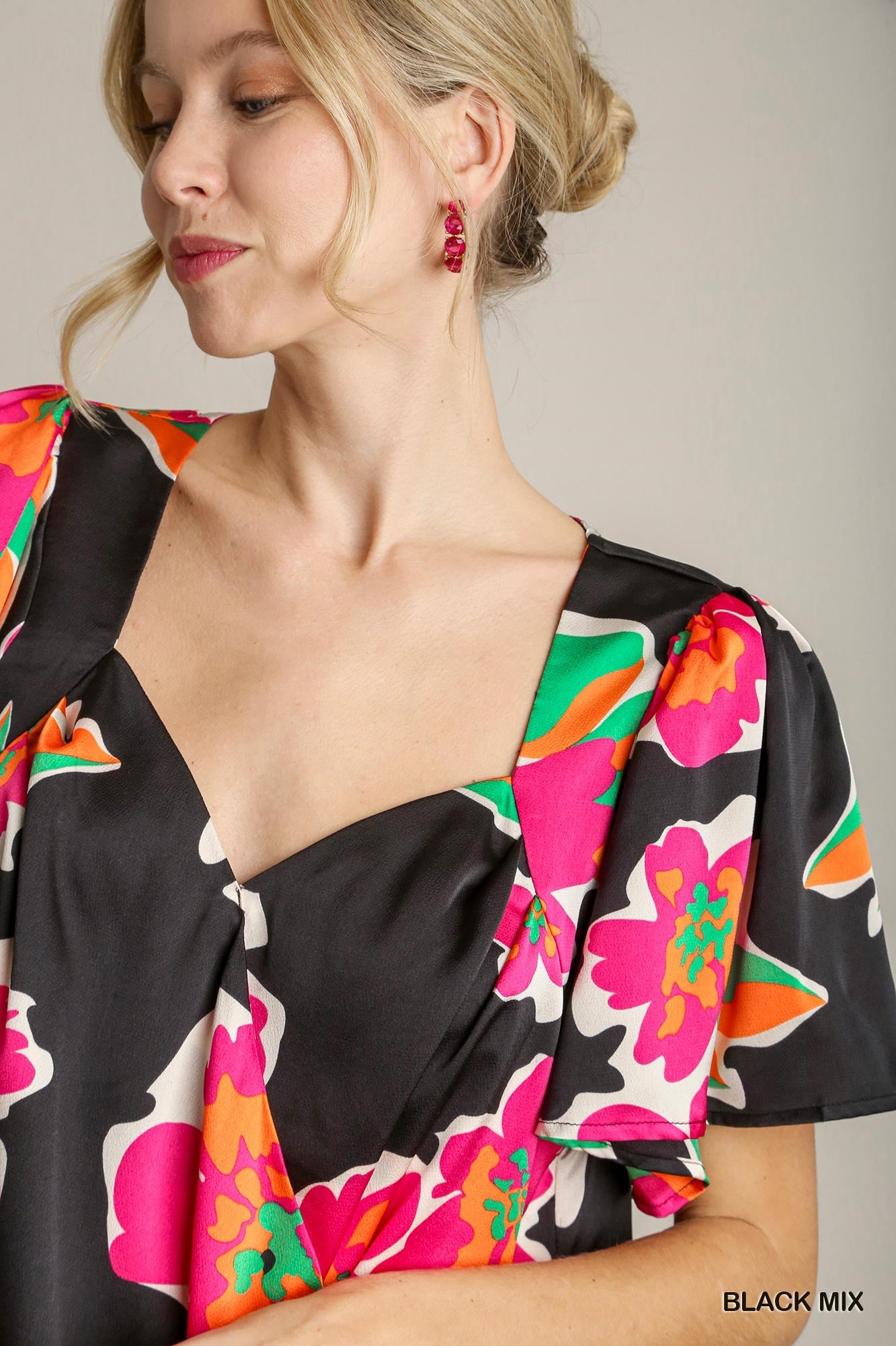 Woman wearing a black floral blouse with colorful patterns on a neutral background