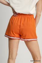 Orange shorts with white trim worn by a person on a plain background