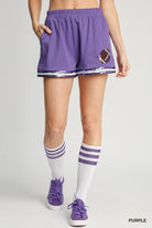 Person wearing purple shorts with a football design, white socks with purple stripes, and purple sneakers on a gray background.