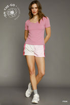 Woman wearing a pink top and white shorts with pink trim against a gray background, featuring 'On-The-Go' branding.