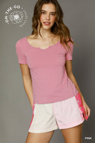 Woman wearing a pink top and white shorts with pink accents, standing against a gray background.