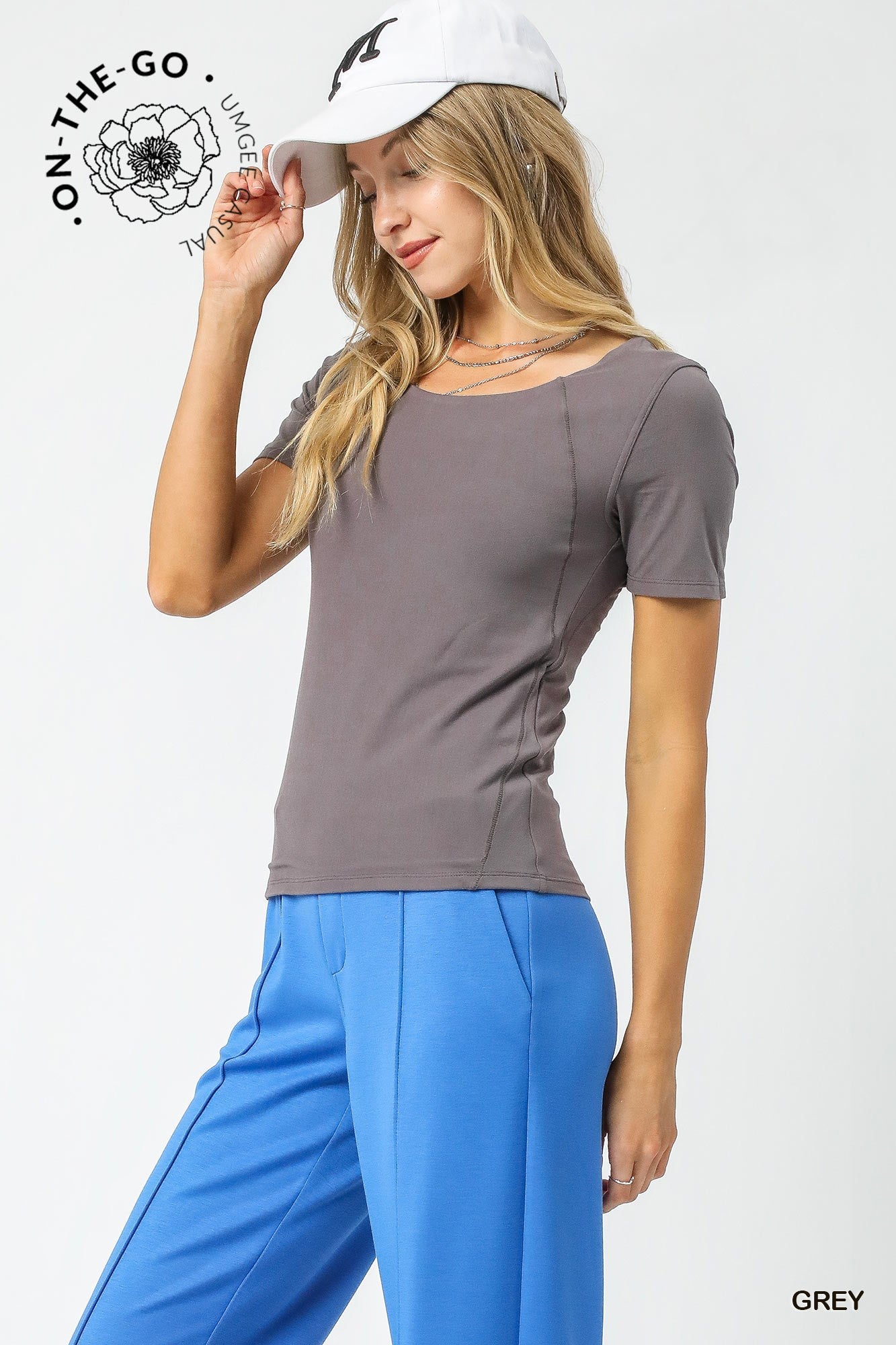 Woman wearing a gray t-shirt and blue pants with a white cap on a light gray background.
