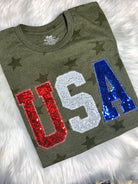 Green t-shirt with 'USA' in red, white, and blue sequins on a fluffy white surface