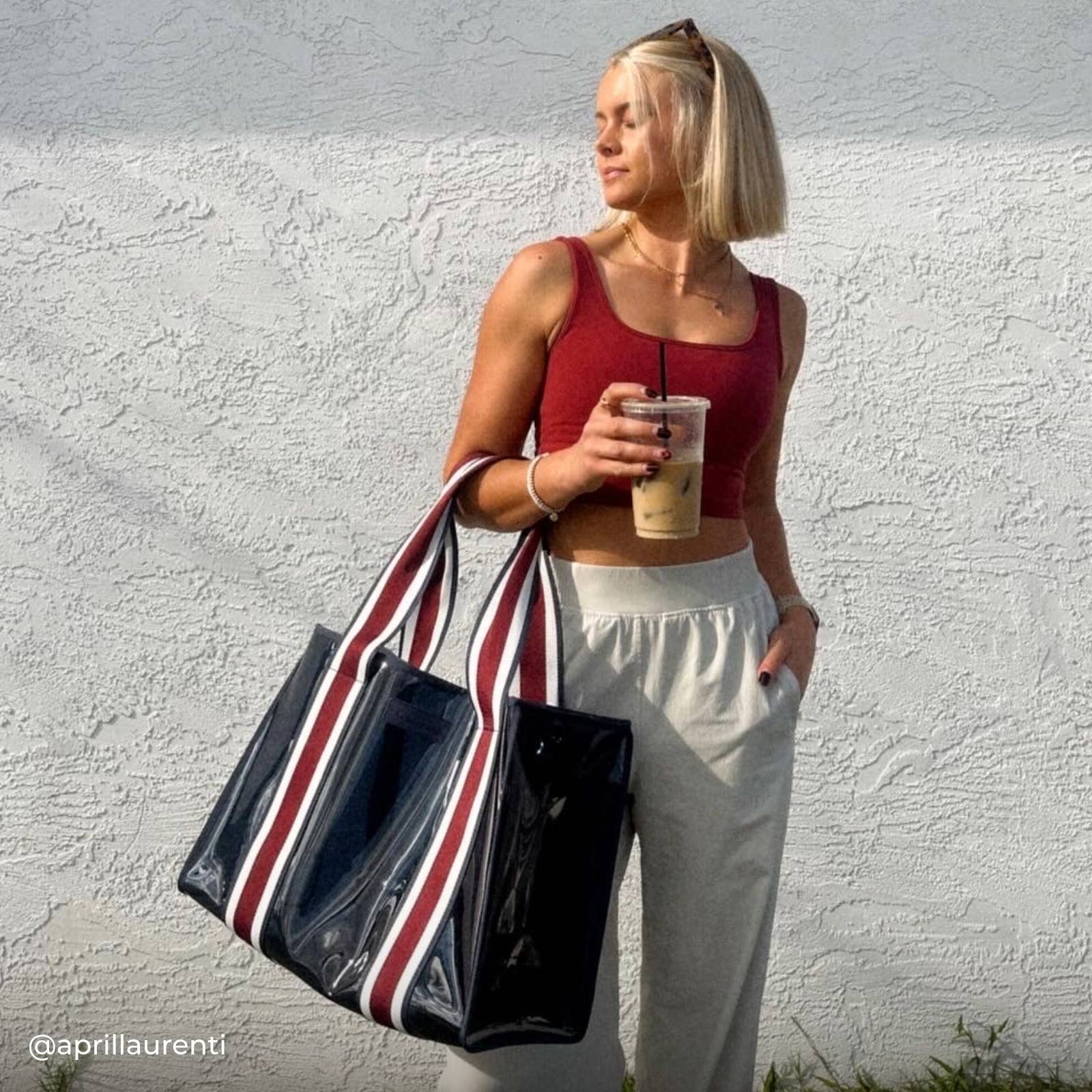 Woman holding a striped bag and a drink against a white wall