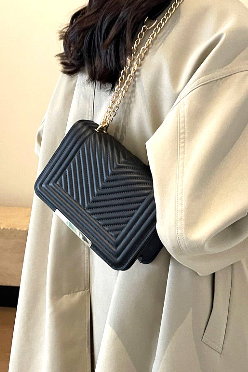 Person wearing a black textured handbag with a gold chain strap.