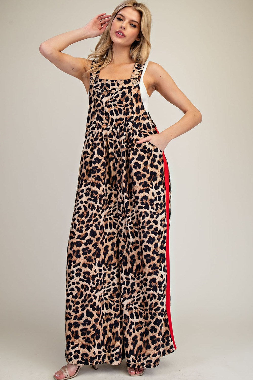 A woman modeling a sleeveless leopard-print maxi dress with a red side stripe, photographed against a plain light beige studio background.