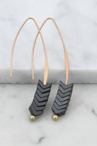 Pair of earrings with black chevron design and gold accents on a marble surface.
