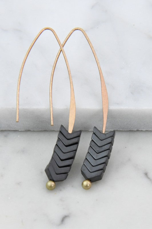 Pair of earrings with black chevron design and gold accents on a marble surface.
