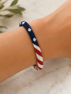 Bracelet with red, white, and blue beads on a wrist against a neutral background