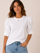 Woman wearing a white blouse with puffed sleeves and blue jeans on a beige background
