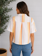 Woman wearing a colorful striped shirt and blue jeans against a gray wall.