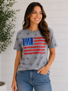 Woman wearing a gray t-shirt with USA flag design against a white wall.