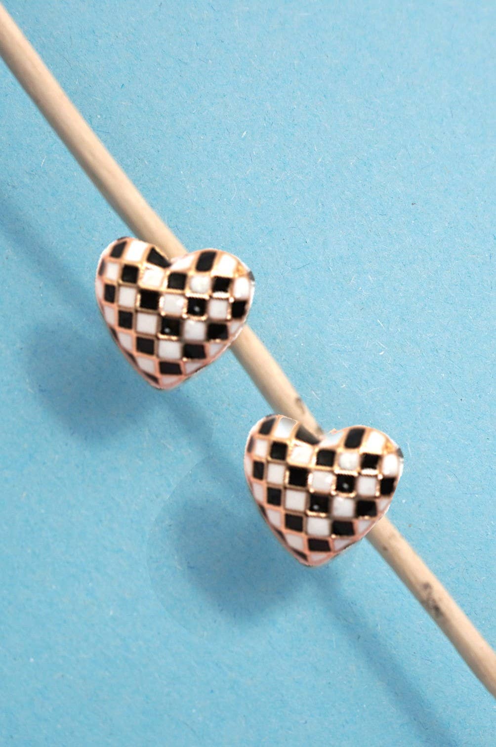 Checkered heart-shaped beads on a wooden stick against a blue background