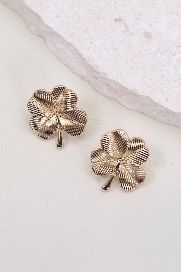 Gold four-leaf clover earrings on a light stone surface