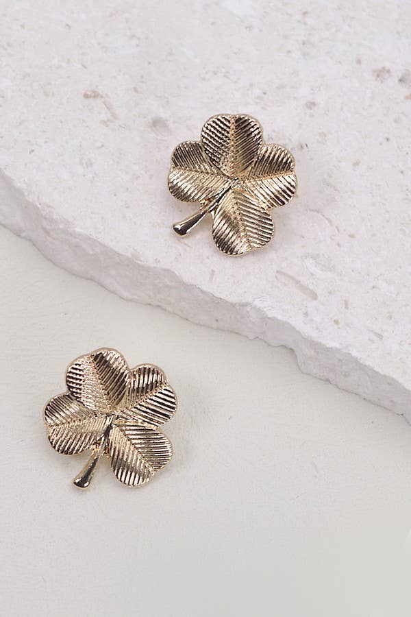 Gold four-leaf clover earrings on a white stone surface