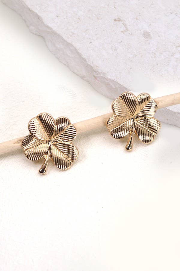 Gold four-leaf clover earrings on a light background