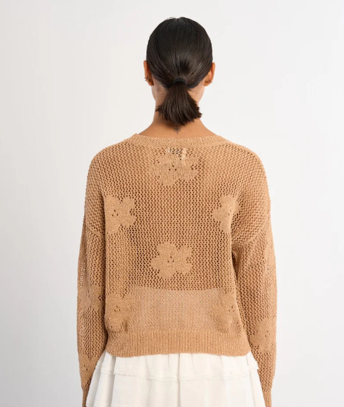 Person wearing a beige knitted sweater with floral patterns on a white background