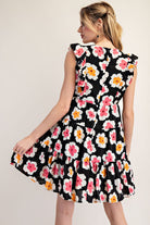 Woman wearing a black sleeveless dress with colorful floral pattern on a plain background