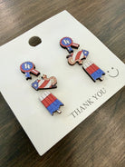 Set of 4th of July themed earrings on a 'THANK YOU' card with a smiley face on a wooden surface