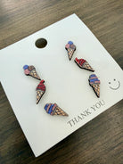 Ice cream cone-shaped earrings on a 'THANK YOU' card with a wooden surface background. Set of 4th of July themed earrings on a 'THANK YOU' card with a smiley face on a wooden surface