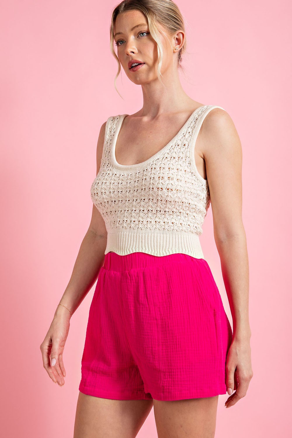 Woman wearing a white sleeveless top and pink shorts against a pink background