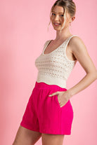 Woman wearing a white crochet top and pink shorts on a pink background