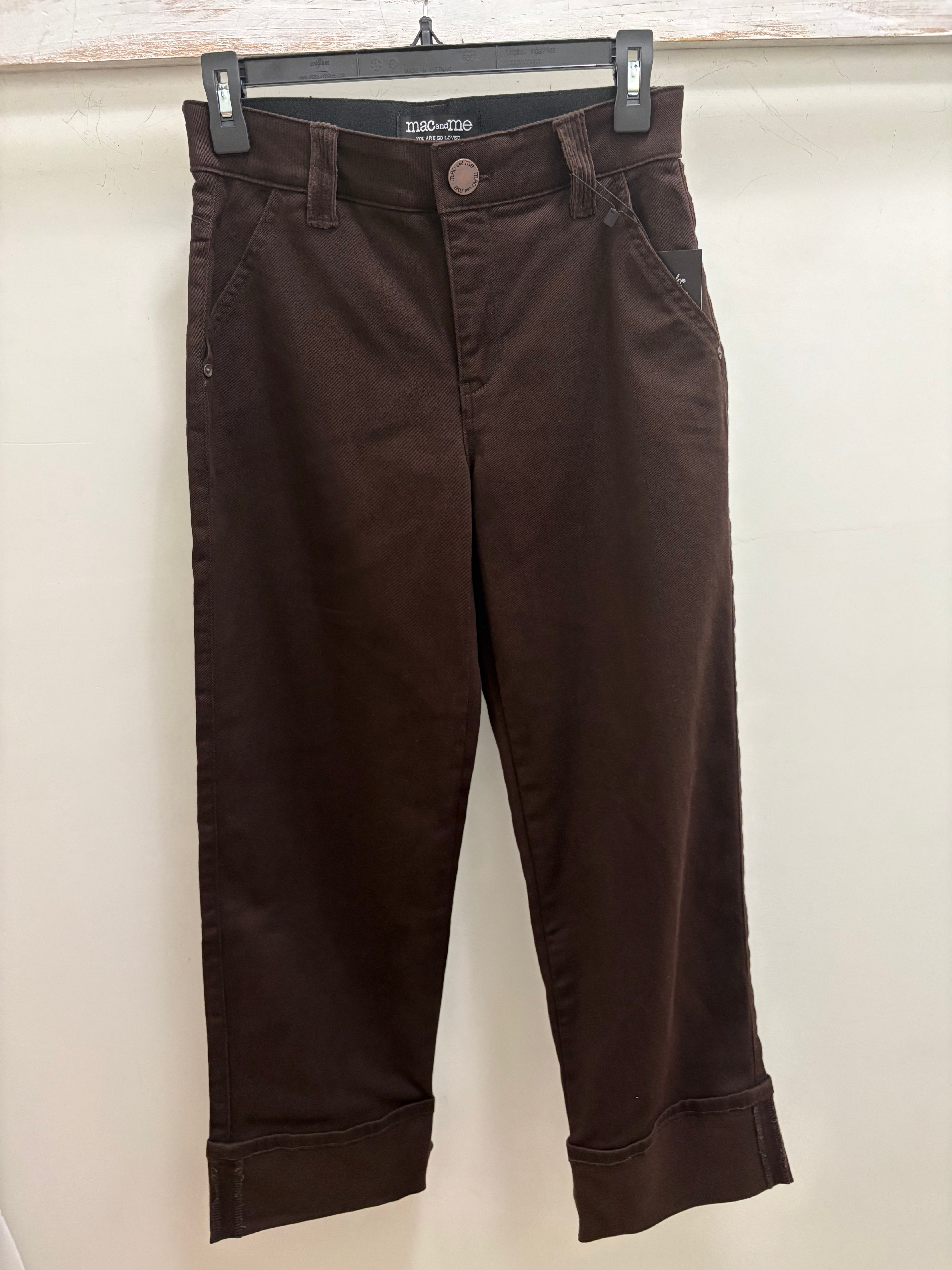 Dark brown cropped pants with rolled cuffs, hanging on a black hanger against a light beige wall.