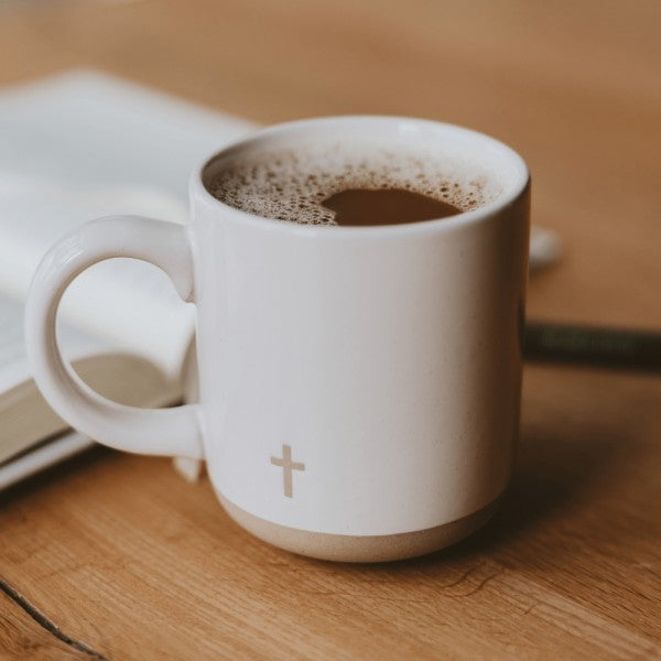 White mug with a cross symbol on a wooden surface, filled with coffee.