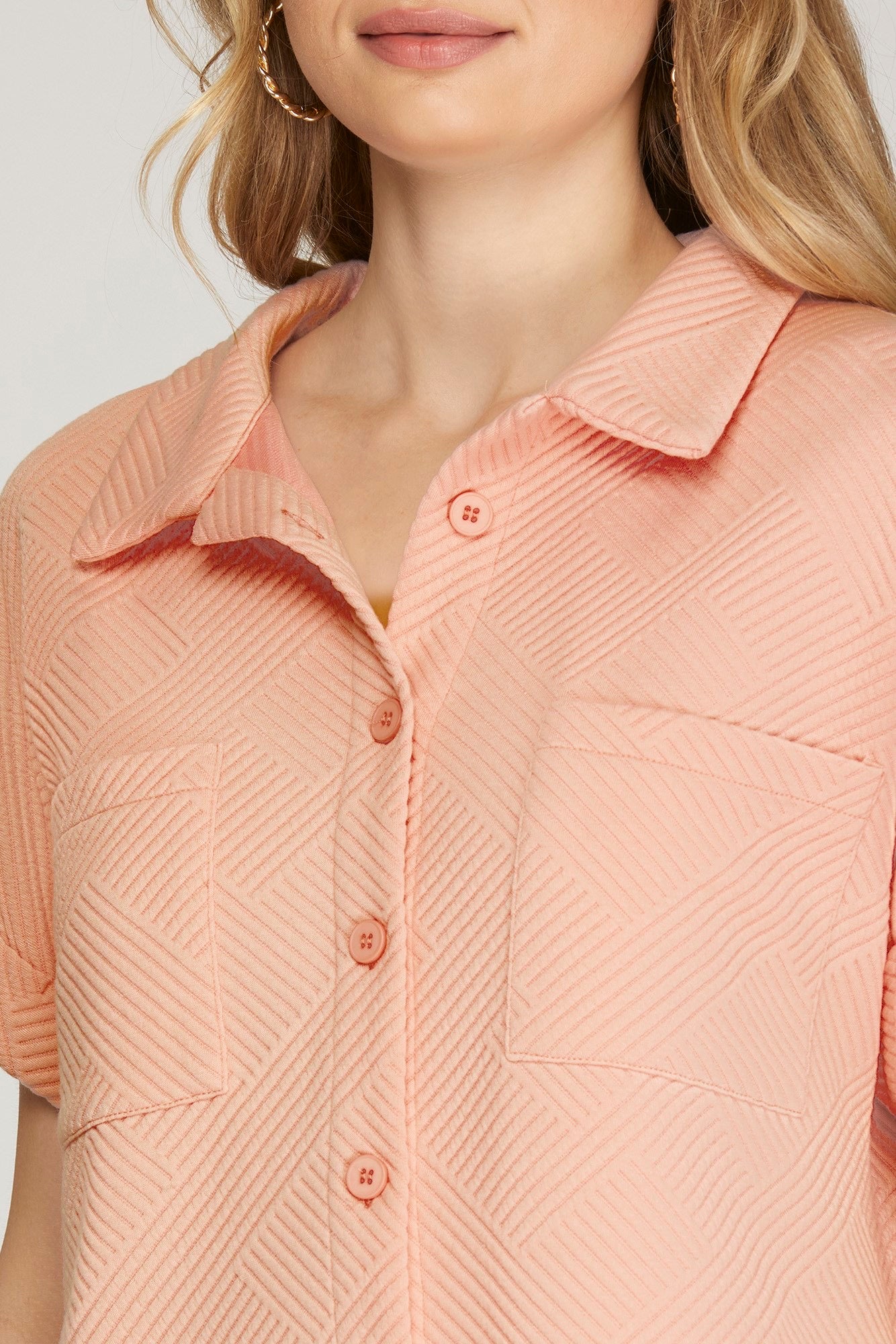 Close-up of a woman wearing a rose-colored short-sleeve button-up shirt with a textured geometric pattern and matching buttons.