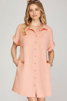 A woman modeling a rose-colored short-sleeve button-up shirt dress with a textured chevron pattern, set against a solid light gray background.