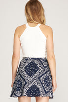 Woman wearing a white top and navy patterned skirt on a plain background