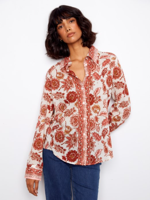 Woman wearing a floral patterned shirt with red and white colors on a plain background